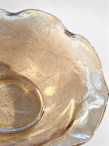 Close-up of molded flowers and leafy vines on the amber glass bowl, with pearlescent reflections along the ruffled rim.