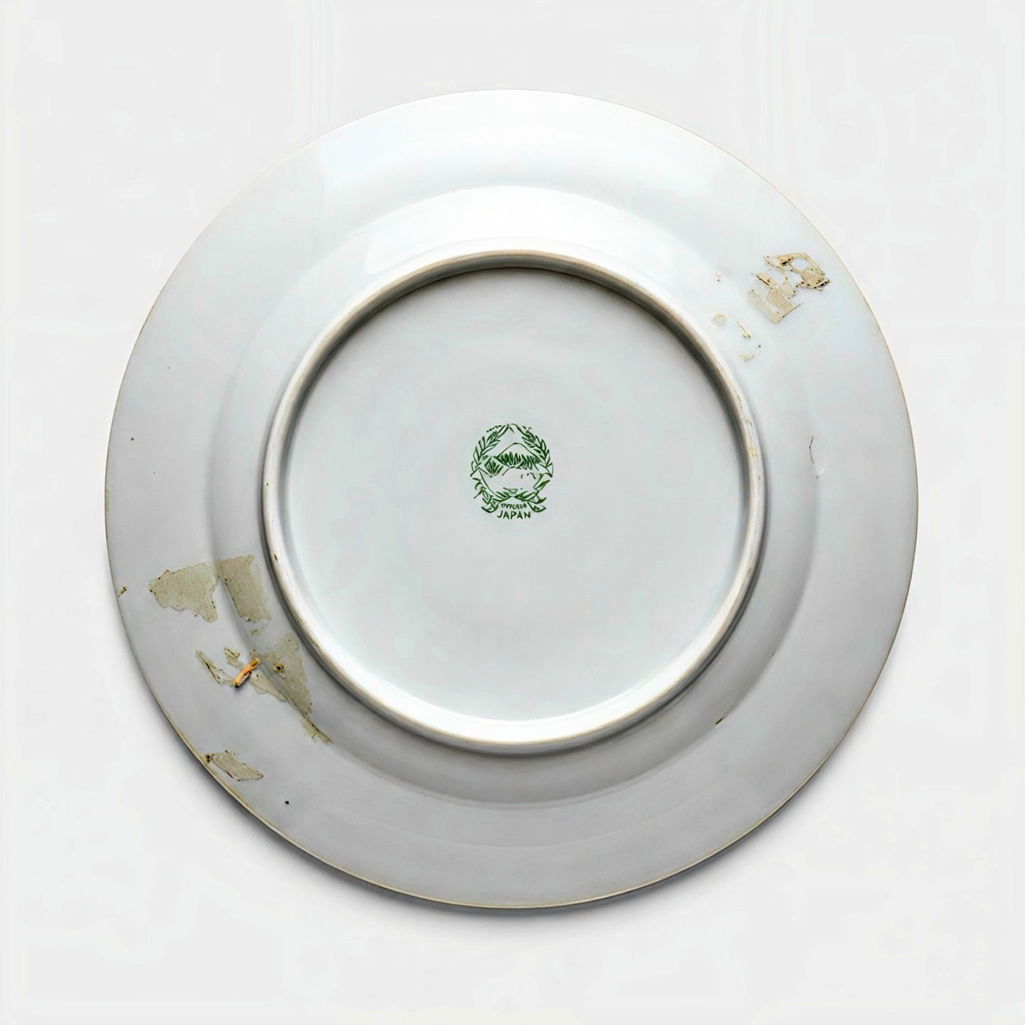 The underside of a vintage porcelain plate showing a green stamped backmark of Mount Fuji inside a wreath, reading Hand Painted Japan, with estate patina.