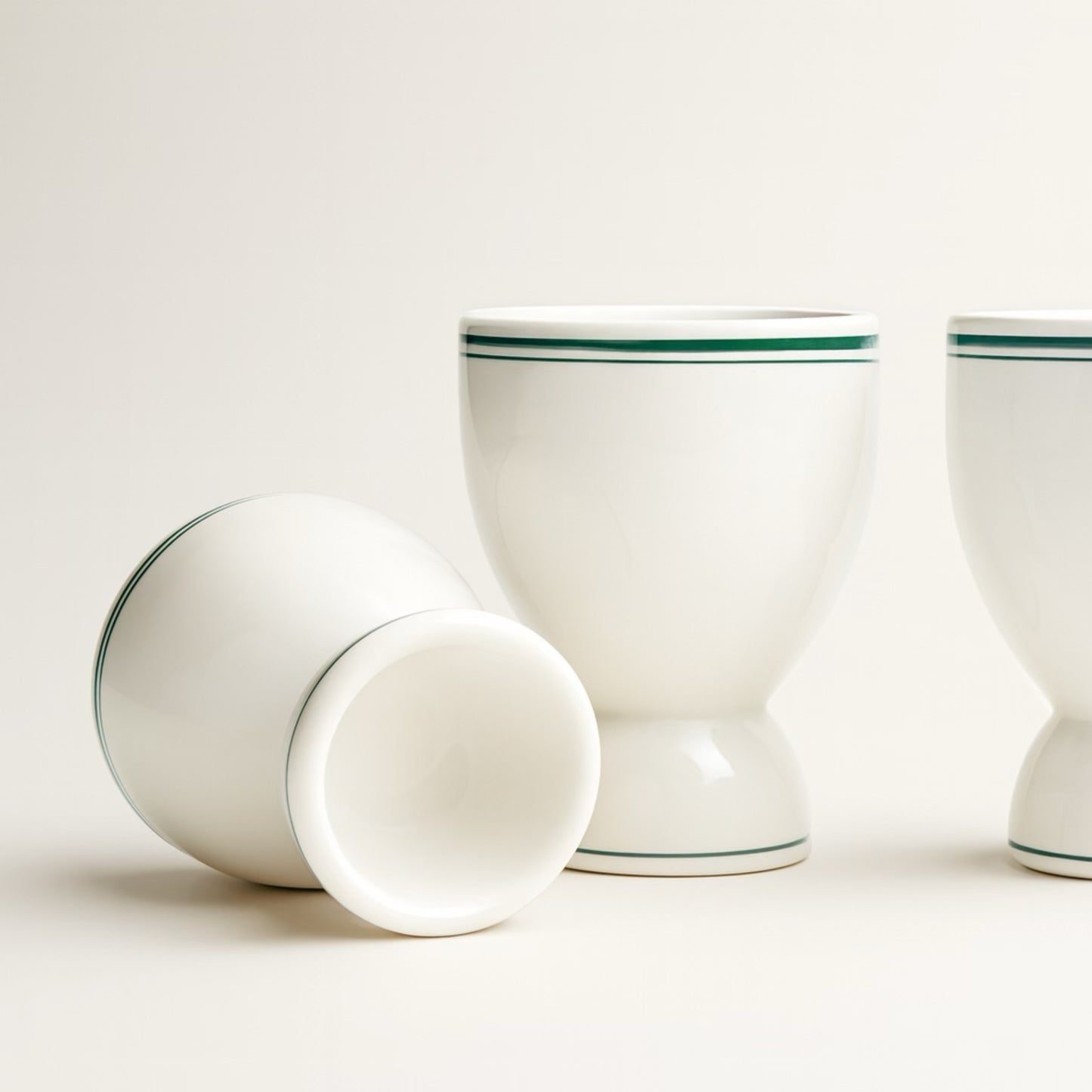Set of three white ceramic egg cups with green stripes, perfect for serving soft-boiled eggs.