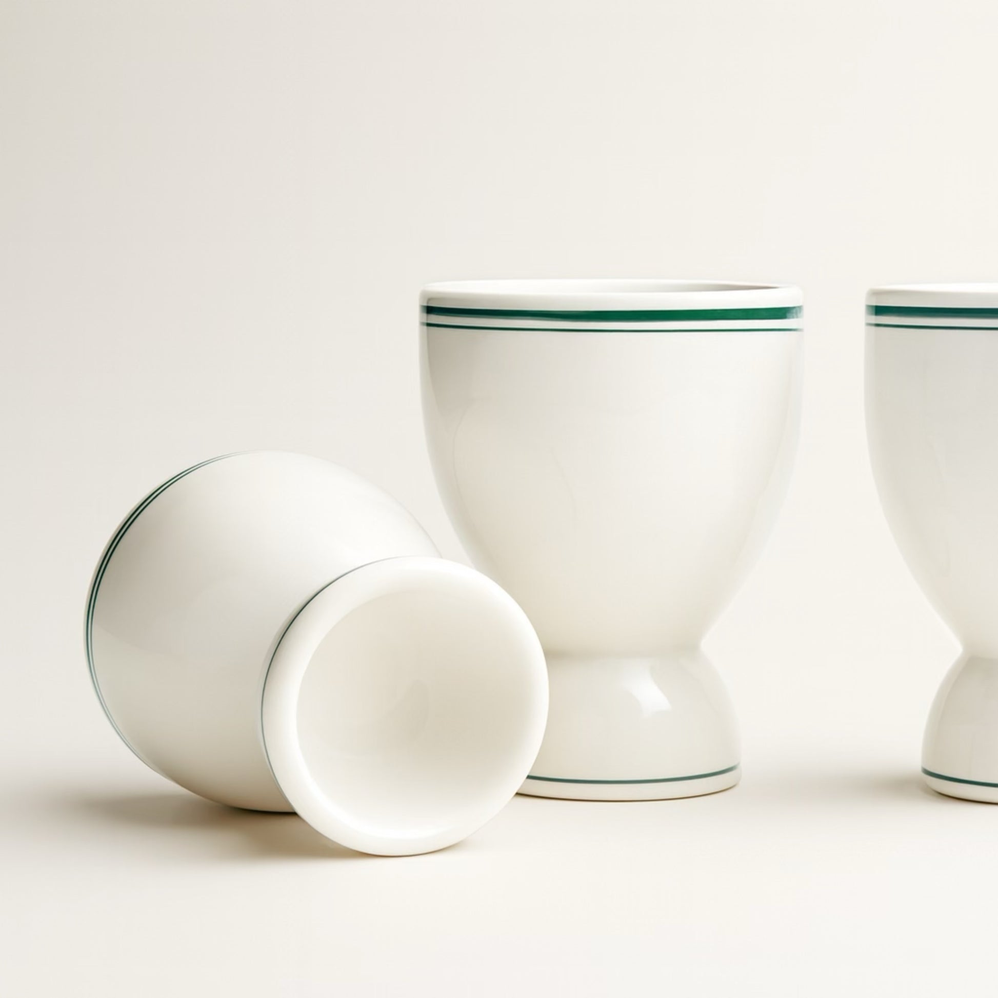 Set of three white ceramic egg cups with green stripes, perfect for serving soft-boiled eggs.
