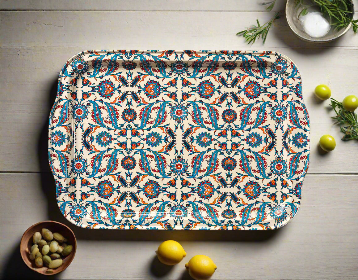 Beste patterned tin serving tray by The Marian Collection styled in a flat lay on a rustic white wood table. The rectangular tray features a vibrant Turkish-inspired symmetrical pattern in teal, cream, and red. It is surrounded by fresh lemons, a small wooden bowl of fava beans, green olives, and rosemary sprigs, showcasing an eclectic kitchen decor style.