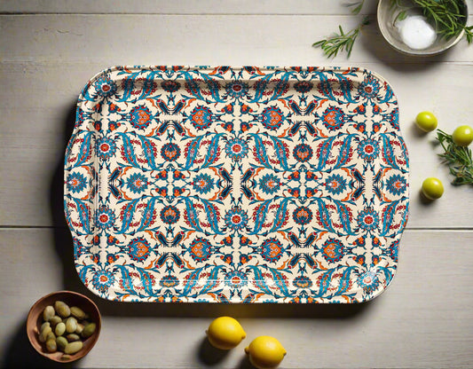 Beste patterned tin serving tray by The Marian Collection styled in a flat lay on a rustic white wood table. The rectangular tray features a vibrant Turkish-inspired symmetrical pattern in teal, cream, and red. It is surrounded by fresh lemons, a small wooden bowl of fava beans, green olives, and rosemary sprigs, showcasing an eclectic kitchen decor style.