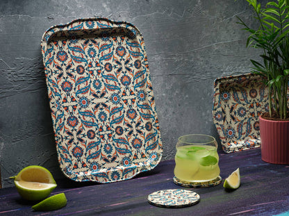 Beste patterned tin serving tray by The Marian Collection styled upright against a textured dark gray wall. This rectangular platter with a vibrant teal and red Turkish motif is paired with a matching coaster, a fresh mint cocktail, lime slices, and a small potted palm, showcasing a moody maximalist bar setup.