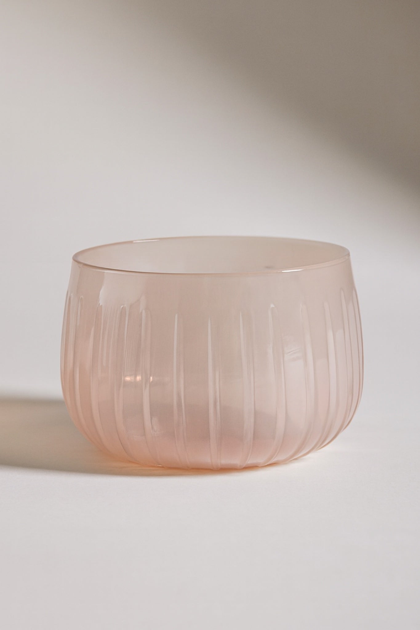 Blush pink ribbed glass bowl with matte finish, styled in soft natural light
