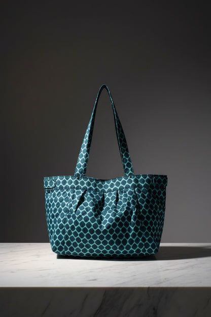 A teal and white patterned tote bag with two shoulder straps, shown floating against a light gray background with a soft shadow underneath.