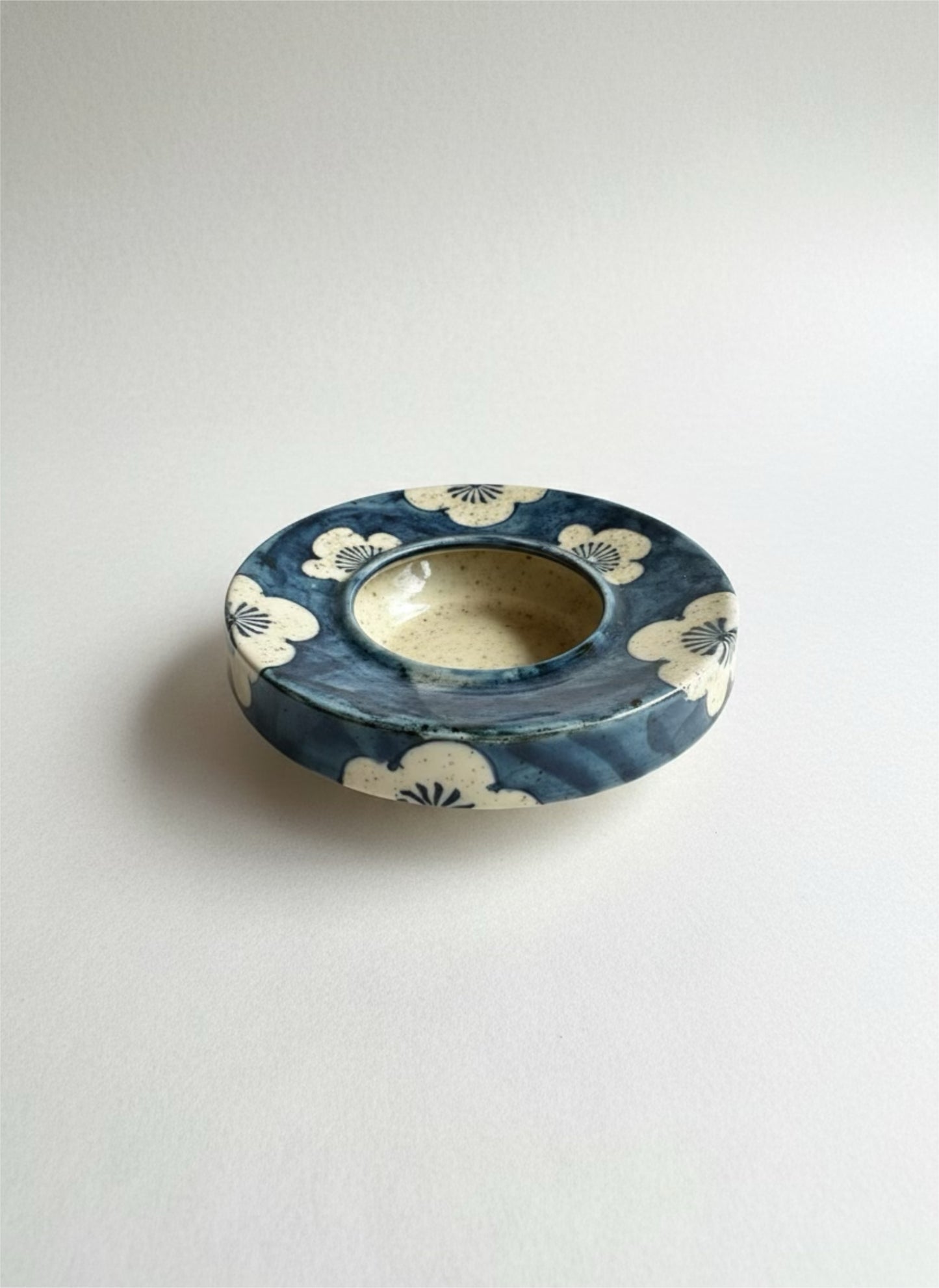 Ceramic plant water retention dish with blue and white design on a light gray background