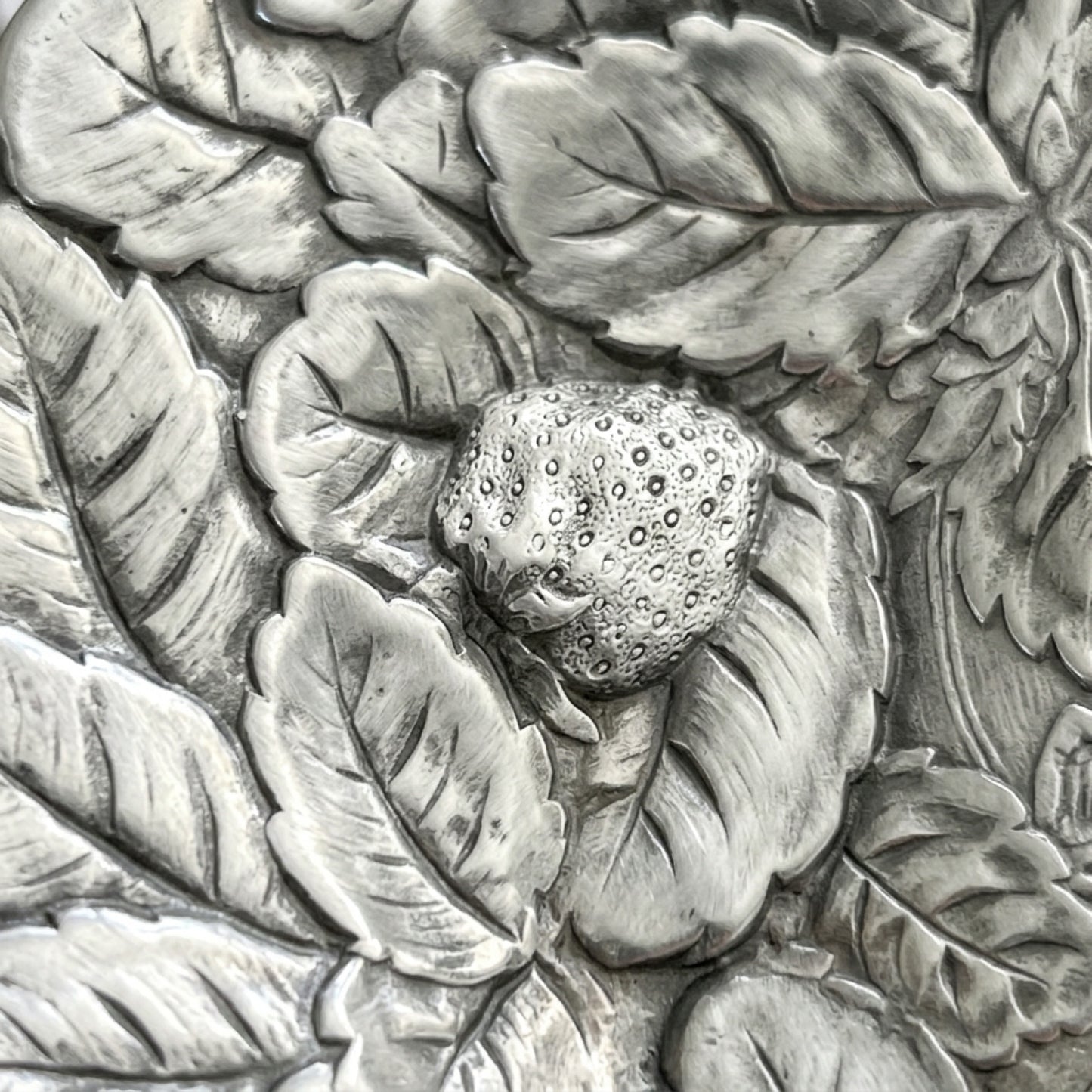 Close up macro detail of the heavy texture and original patina on a scalloped edge silver serving platter with a fruit motif.
