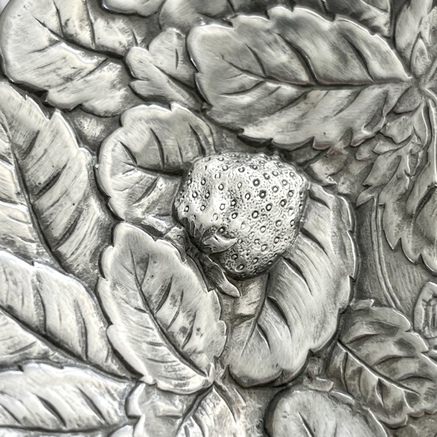 Close up macro detail of the heavy texture and original patina on a scalloped edge silver serving platter with a fruit motif.