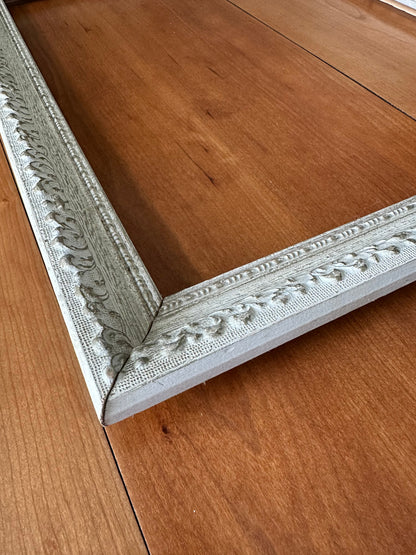 Vintage carved wood picture frame laid flat on a wood surface showing profile depth, double-tiered molding, and slate blue French grey finish with gilt accents