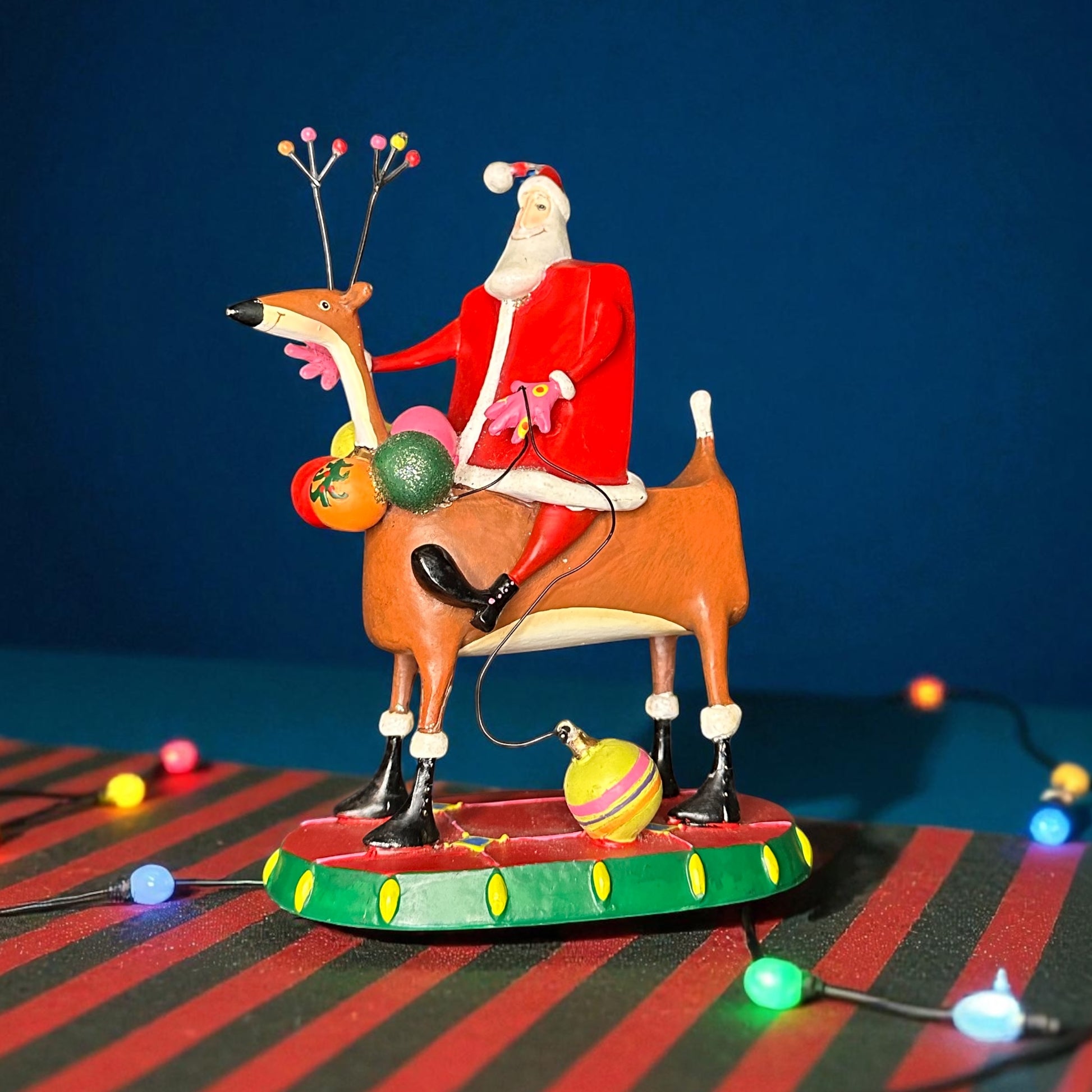 Decorative figurine of Santa Claus riding a reindeer with Christmas lights on a striped surface.