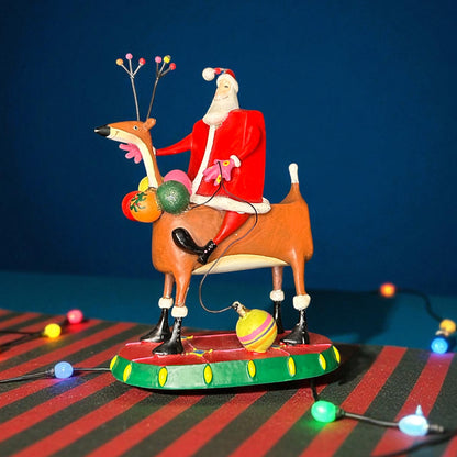 Decorative figurine of Santa Claus riding a reindeer with Christmas lights on a striped surface.