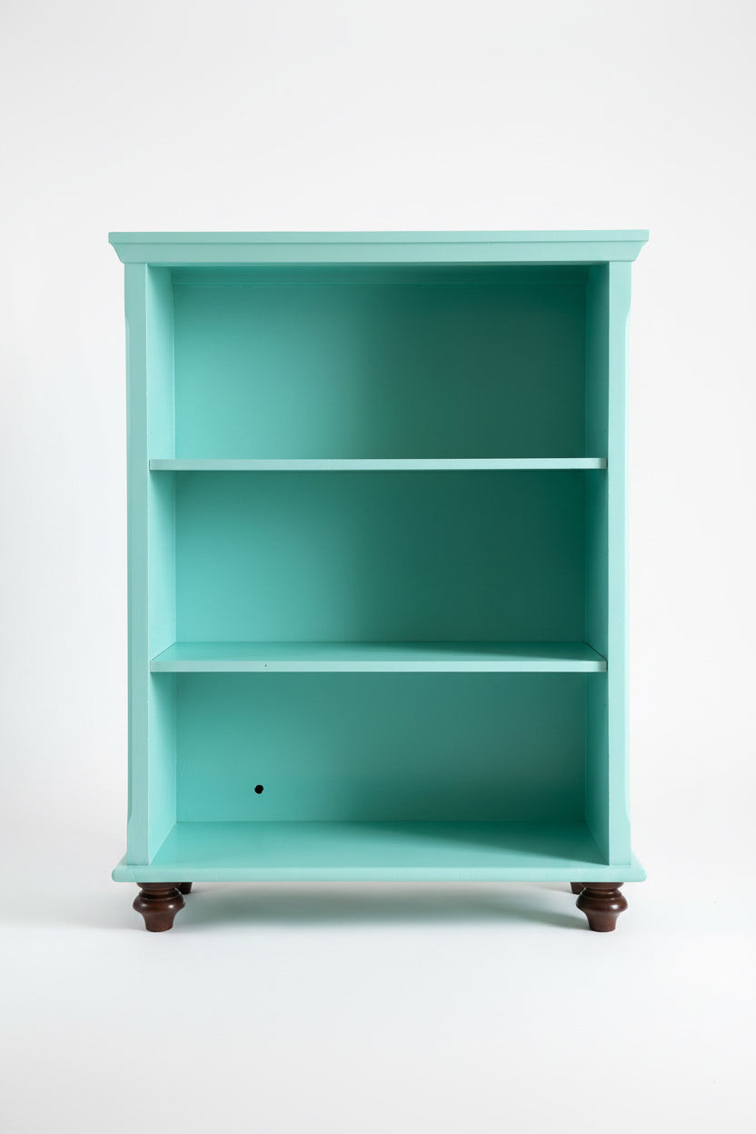 Front view of a solid wood bookcase hand-painted in Fusion Mineral Paint's Laurentine teal colorway. The three-shelf wooden bookcase features a smooth, satin poly-acrylic finish and is structurally elevated on four dark espresso-toned turned hardwood feet. Set against a clean, minimalist white studio background to highlight the bold-eclectic statement design by The Marian Collection.