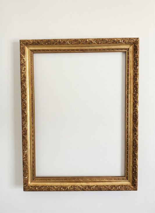 Front view of an empty vintage ornate picture frame from The Marian Collection, finished in a deep antiqued gilded gold with heavy scrollwork detailing. Outer dimensions measure 27.5 x 22 inches, designed to fit 24 x 18 inch art prints or landscape canvases. Beautiful addition for modern heritage and maximalist wall decor.