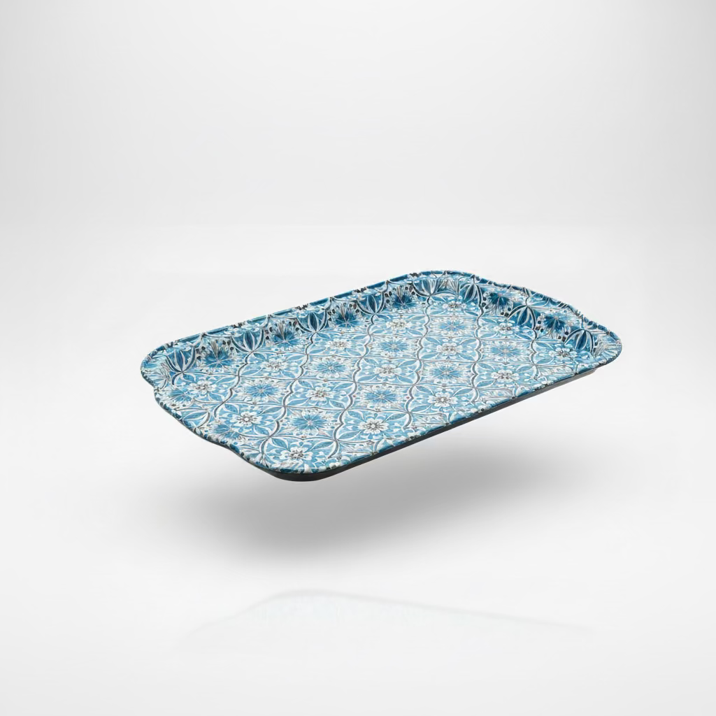 A rectangular decorative tray with a blue and white floral pattern, resting on a black laptop on a wooden table with a window and wooden fence in the background.