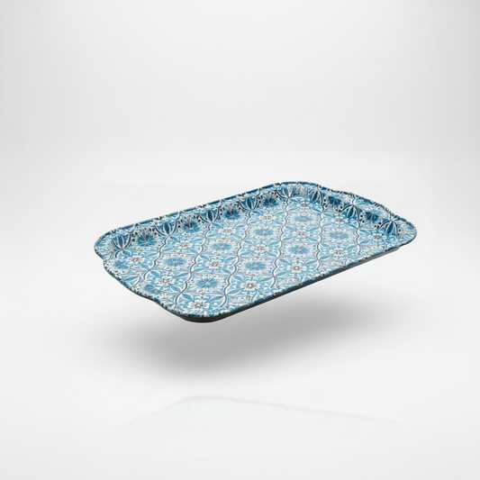 A rectangular decorative tray with a blue and white floral pattern, resting on a black laptop on a wooden table with a window and wooden fence in the background.