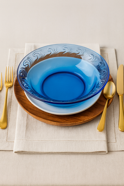 Blue glass bowl on a wooden plate with gold cutlery on a beige tablecloth.
