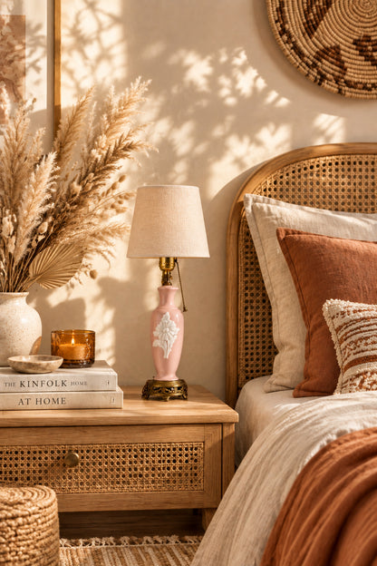 Full view of a vintage blush pink porcelain table lamp featuring a white relief flower motif, brass pull chain, and ornate brass footed base.