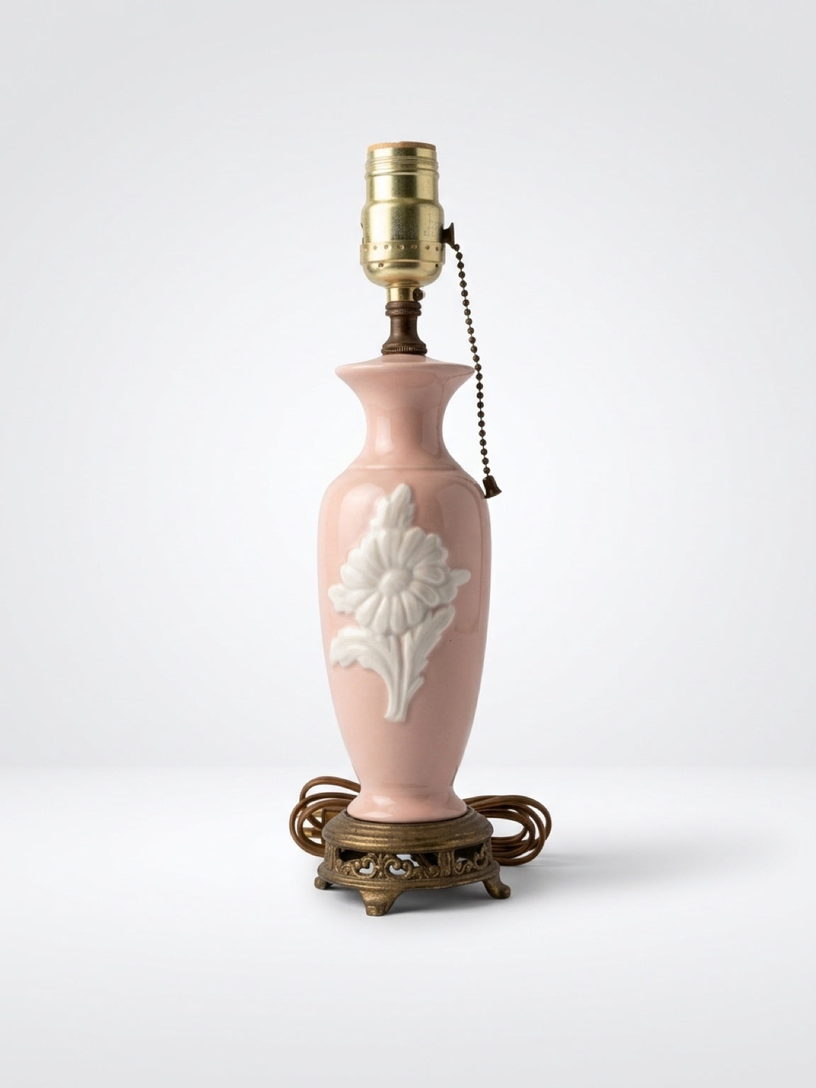 Vintage blush pink ceramic boudoir table lamp with embossed white flower relief, pull chain, and ornate brass footed base.