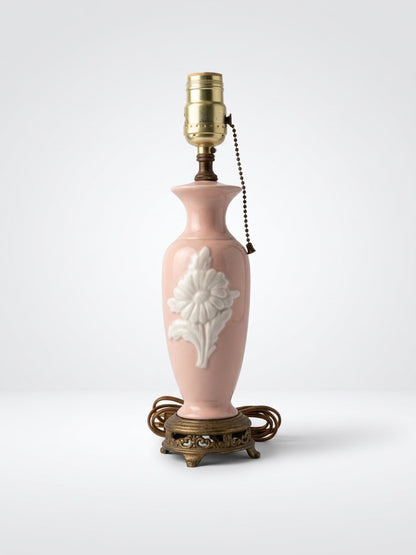 Vintage blush pink ceramic boudoir table lamp with embossed white flower relief, pull chain, and ornate brass footed base.