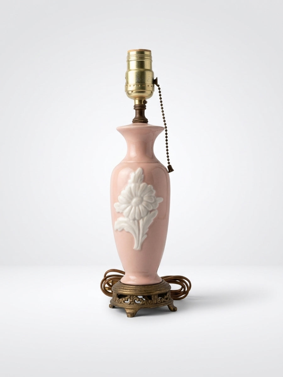 Vintage blush pink ceramic boudoir table lamp with embossed white flower relief, pull chain, and ornate brass footed base.