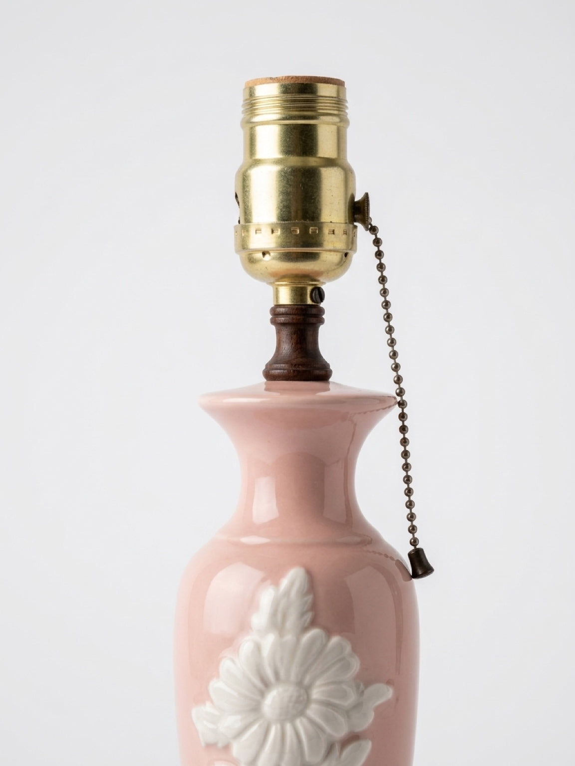 Close-up view of the brass light socket, brown wooden neck accent, and pull-chain switch of a vintage blush pink porcelain table lamp.