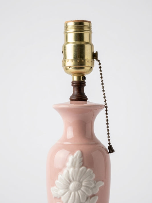 Close-up view of the brass light socket, brown wooden neck accent, and pull-chain switch of a vintage blush pink porcelain table lamp.