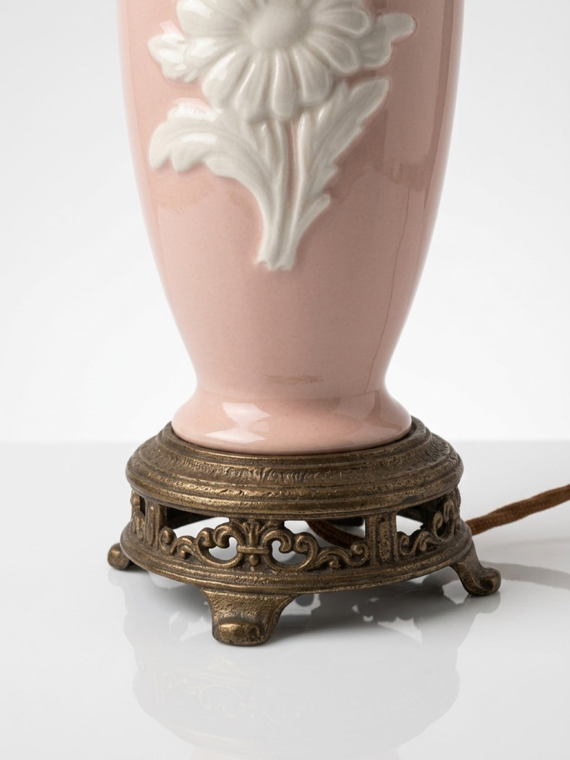 Close-up detail of the ornate, filigree brass base and power cord attachment on a vintage pink porcelain lamp.
