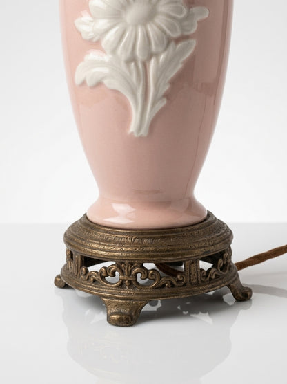 Close-up detail of the ornate, filigree brass base and power cord attachment on a vintage pink porcelain lamp.