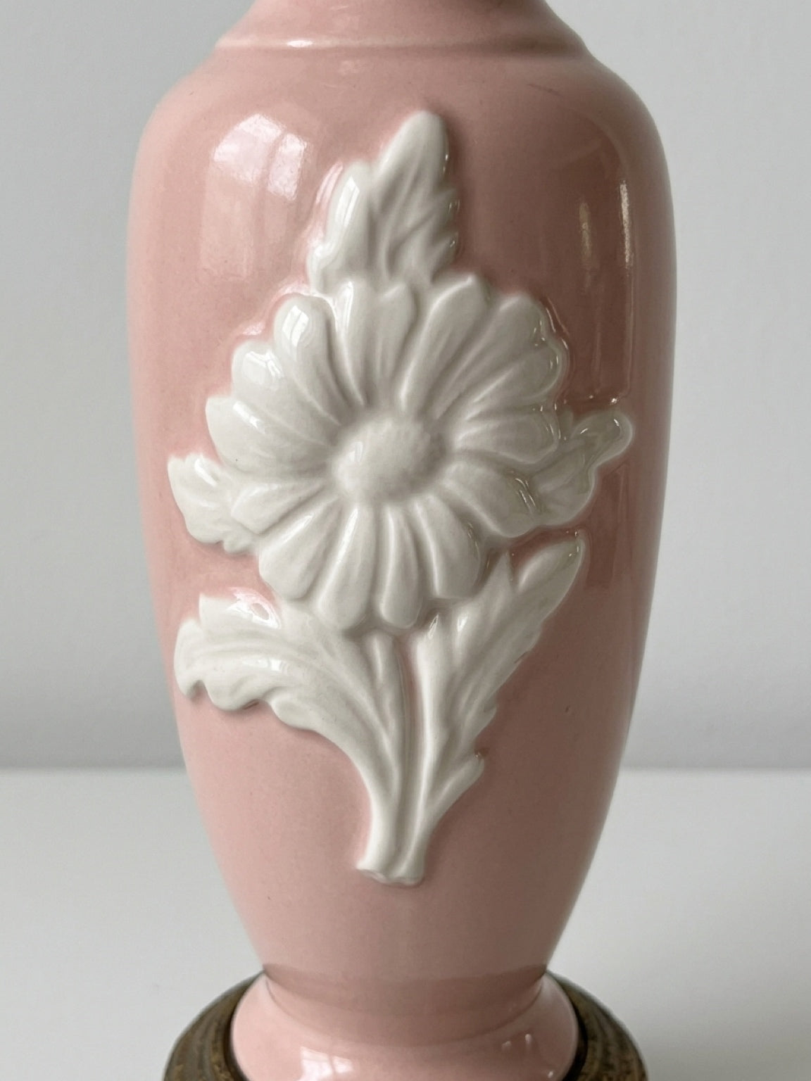 Close-up detail of the white embossed floral motif on the glossy pink ceramic body of a vintage table lamp.