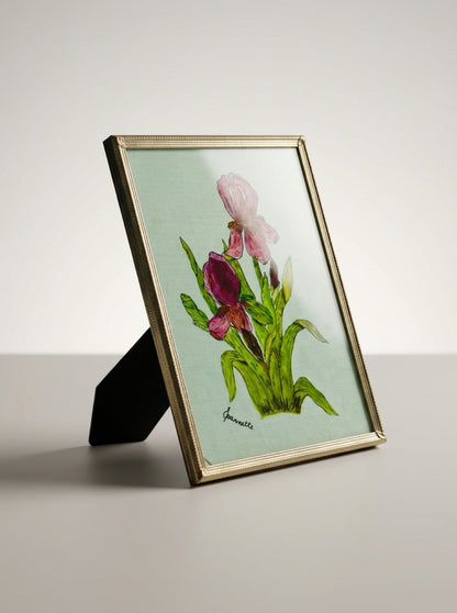 Signed Jeannette iris artwork in a beaded brass-tone frame, shown at an angle with its black easel support visible.