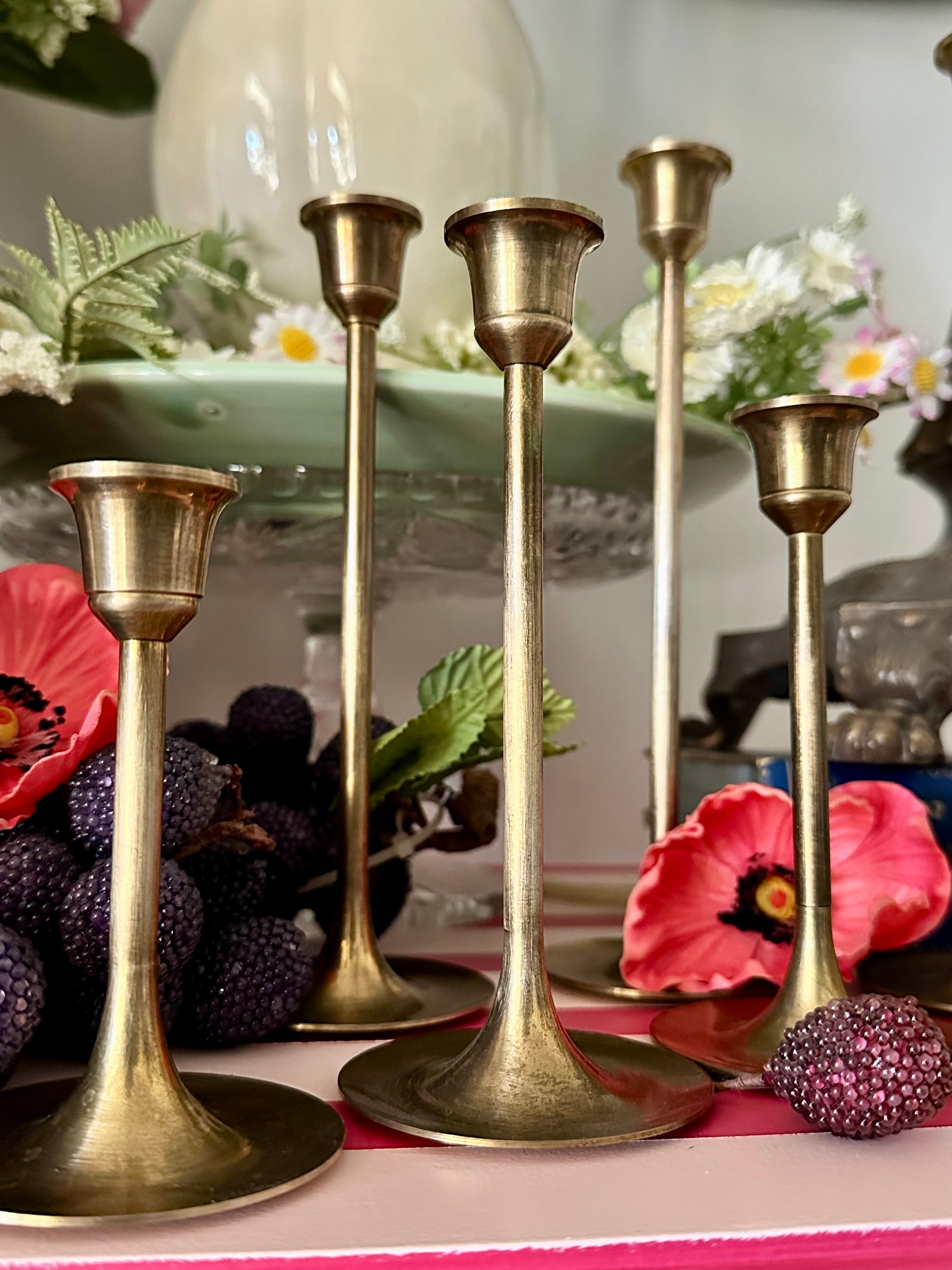 Set of gold candle holders on a decorative table with flowers and fruit.
