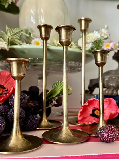 Set of gold candle holders on a decorative table with flowers and fruit.
