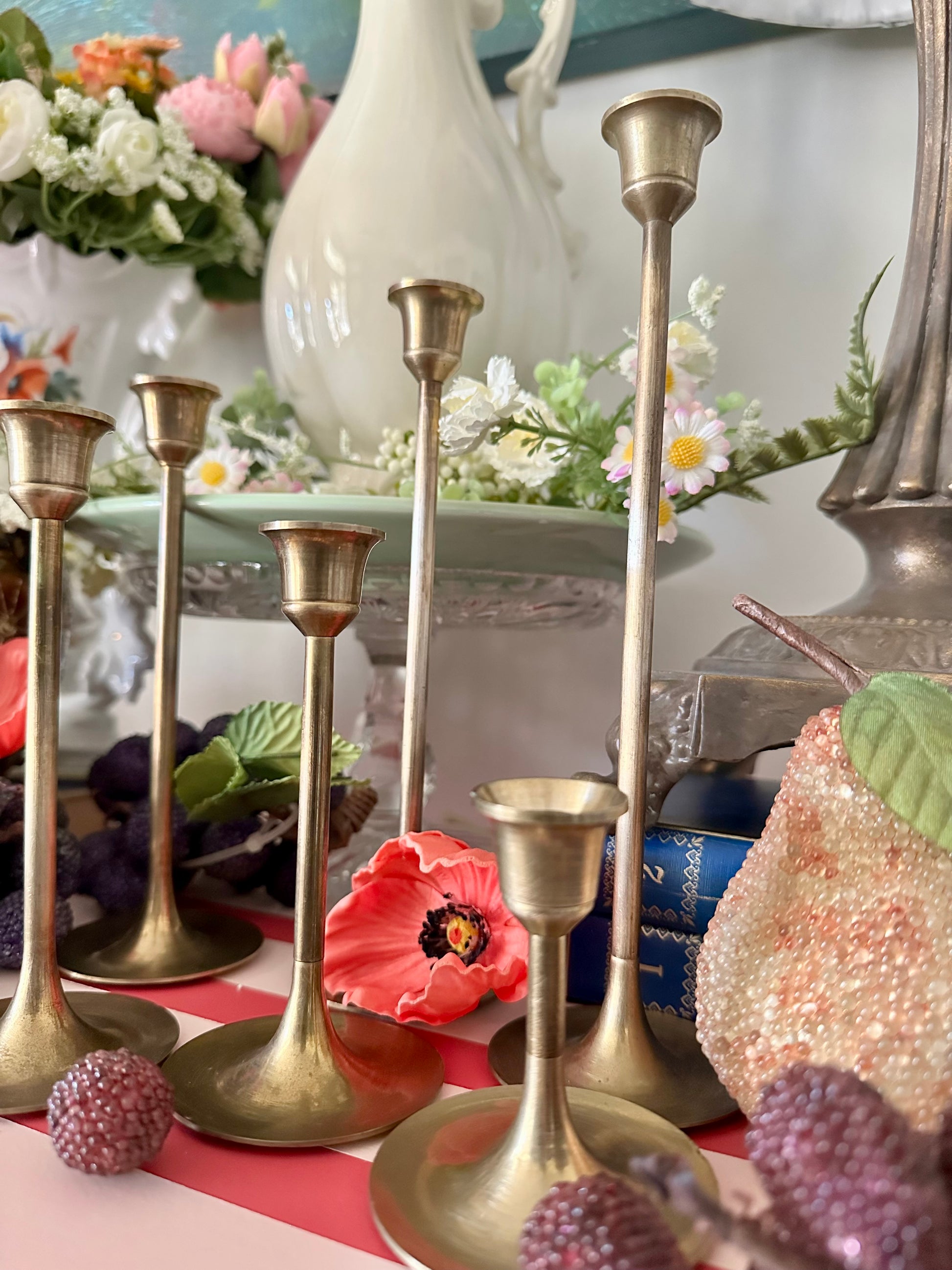 Gold candlesticks on a table with decorative items and flowers in the background