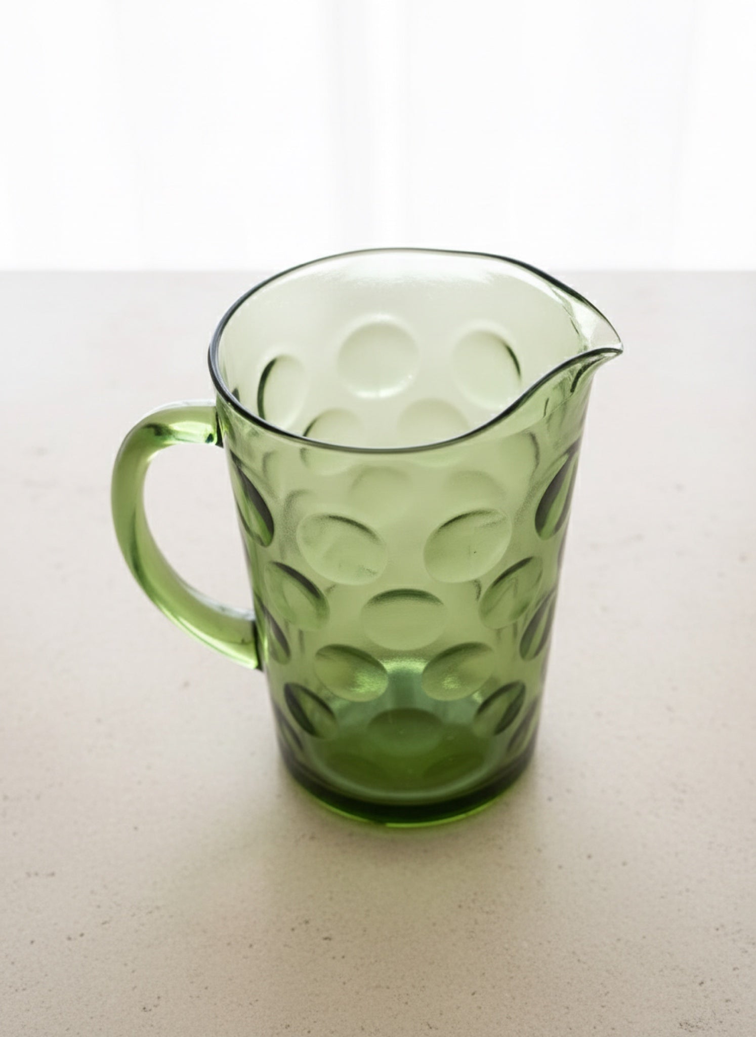 Mid Century Modern Green glass pitcher with a circle "thumbprint" pattern on a white surface