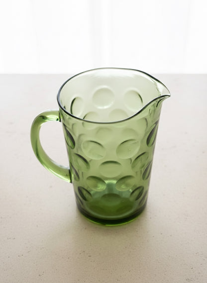 Mid Century Modern Green glass pitcher with a circle "thumbprint" pattern on a white surface