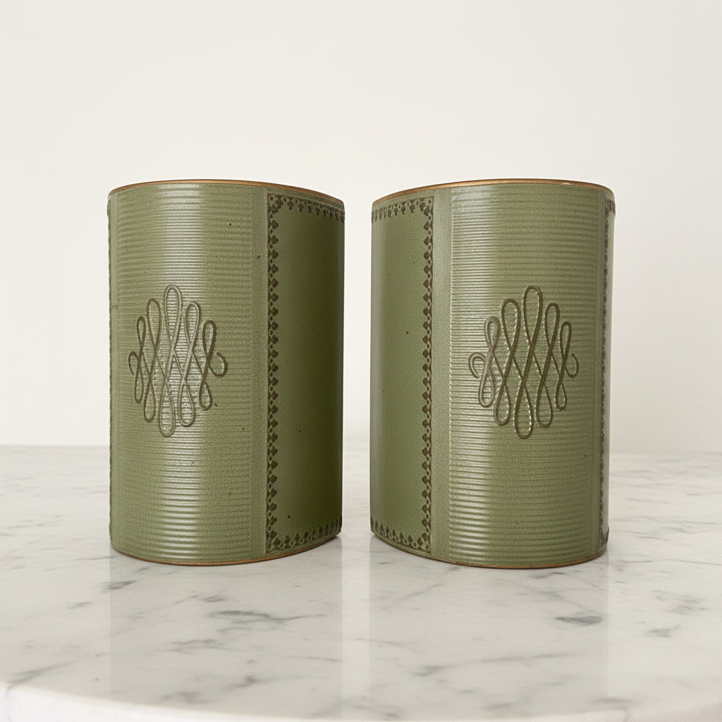 Pair of vintage mid-century sage green leather bookends featuring gold-tooled borders and central scroll monogram, displayed on a white marble surface.