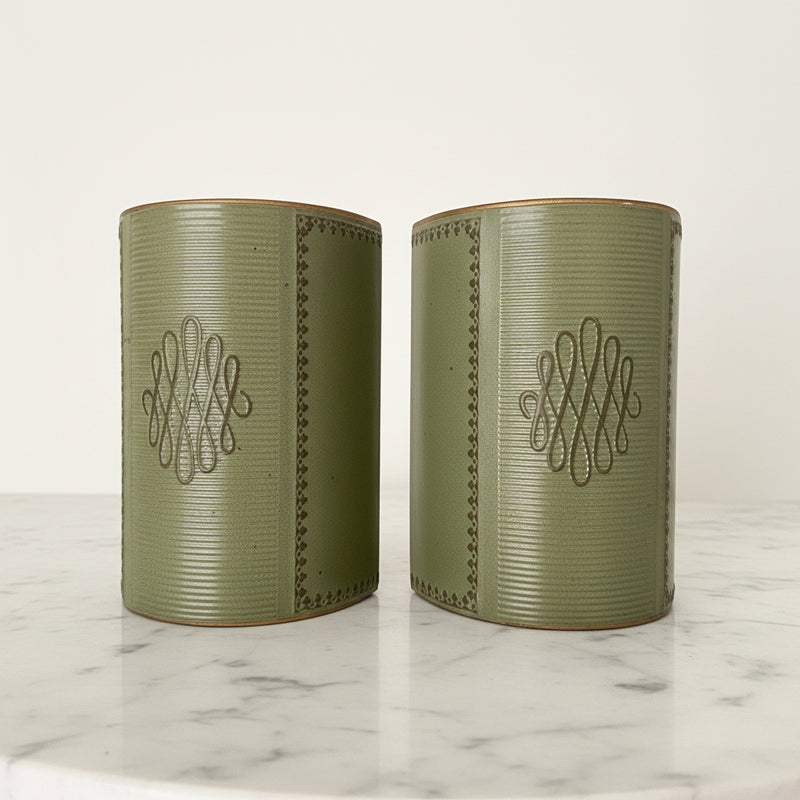 Pair of vintage mid-century sage green leather bookends featuring gold-tooled borders and central scroll monogram, displayed on a white marble surface.