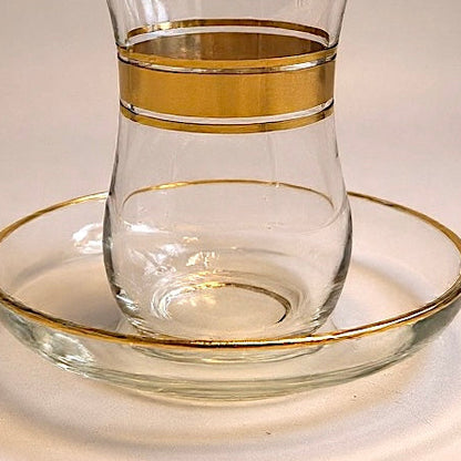 Clear glass tumbler with gold band on a matching glass coaster against a neutral background