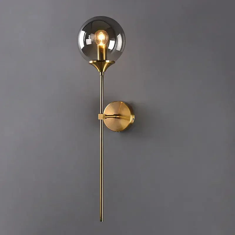 Wall-mounted lamp with gold fixture and glass shade on a gray wall