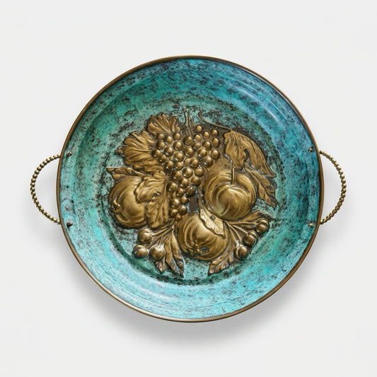 Top-down studio shot of a vintage Italian round brass tray on a white background, featuring a heavy-relief embossed fruit motif of grapes and peaches centered on a striking, textured turquoise-green verdigris patina with delicate beaded brass side handles.