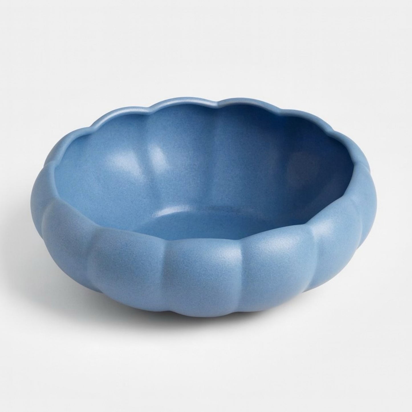 Top-down view of a sculptural blue ceramic bowl with rounded lobes and a matte glaze. The fluted design evokes floral and organic shapes, styled for modern vintage interiors.