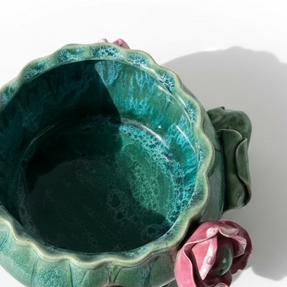 Top down view of a vintage green majolica style ceramic planter bowl showing mottled teal drip glaze interior and dimensional pink lotus flower on the edge.