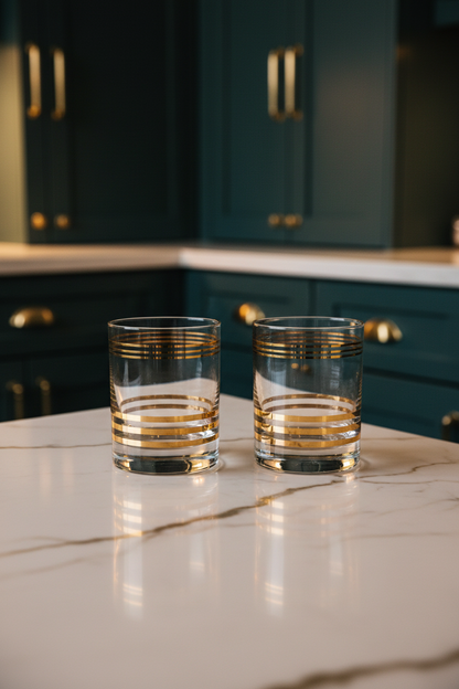 Mid-Century Modern Hand-Blown Gold Banded Rocks Glasses | Set of 2. lifestyle image sitting on marble countertop with dark teal painted cabinets in the background 
