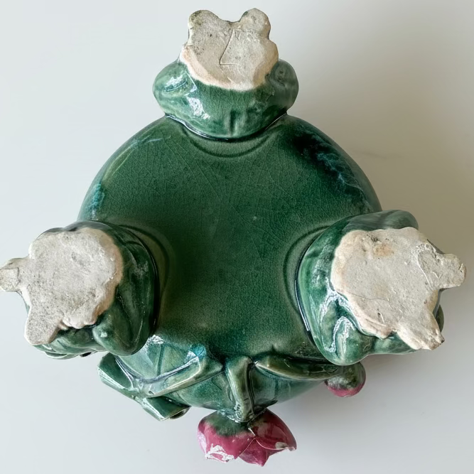 Unglazed bottom pads of three figural ceramic frog feet supporting a vintage majolica planter, showing a handwritten incised artisan character mark.