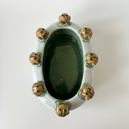 Vintage majolica style oval ceramic planter with eight molded frogs on green lily pads around the rim, white body with a brown faux-bois tree stump base.⁠