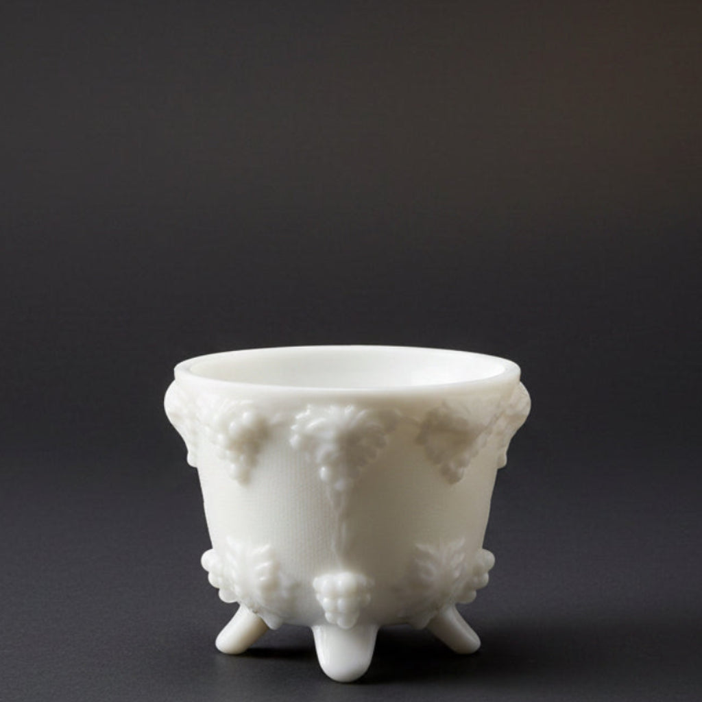 Vintage white milk glass footed cachepot with an embossed grapevine and grape cluster motif, centered against a dark gray background.