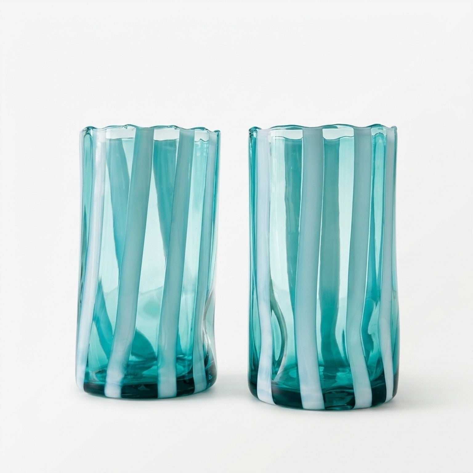 Pair of Alessandro Coppola for Vetreria Arte di Murano hand-blown Italian glass tumblers featuring aqua blue and milky white vertical stripes styled on a warm wood surface.