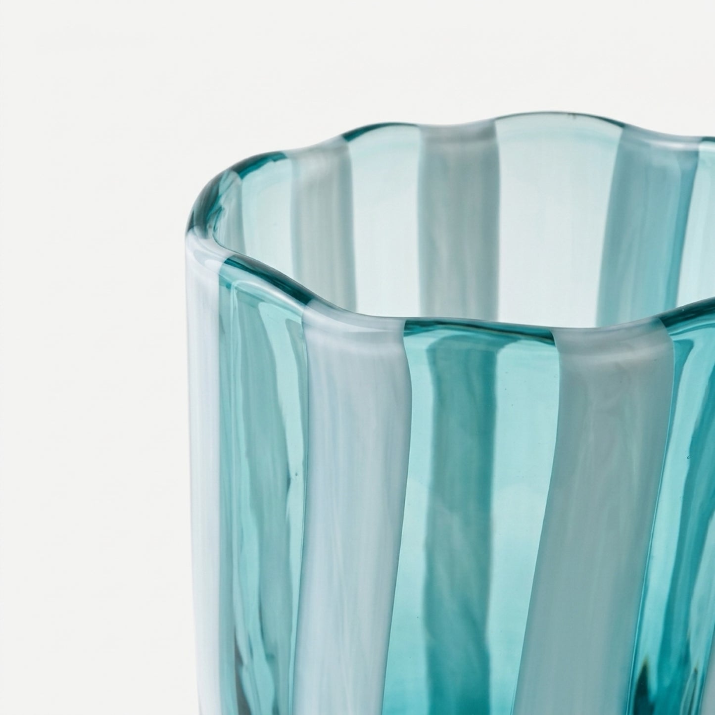 A macro close-up shot highlighting the undulating, wavy rim and thick, hand-blown texture of an Alessandro Coppola for Vetreria Arte di Murano aqua and white vertical candy-striped glass tumbler on a bright white background.