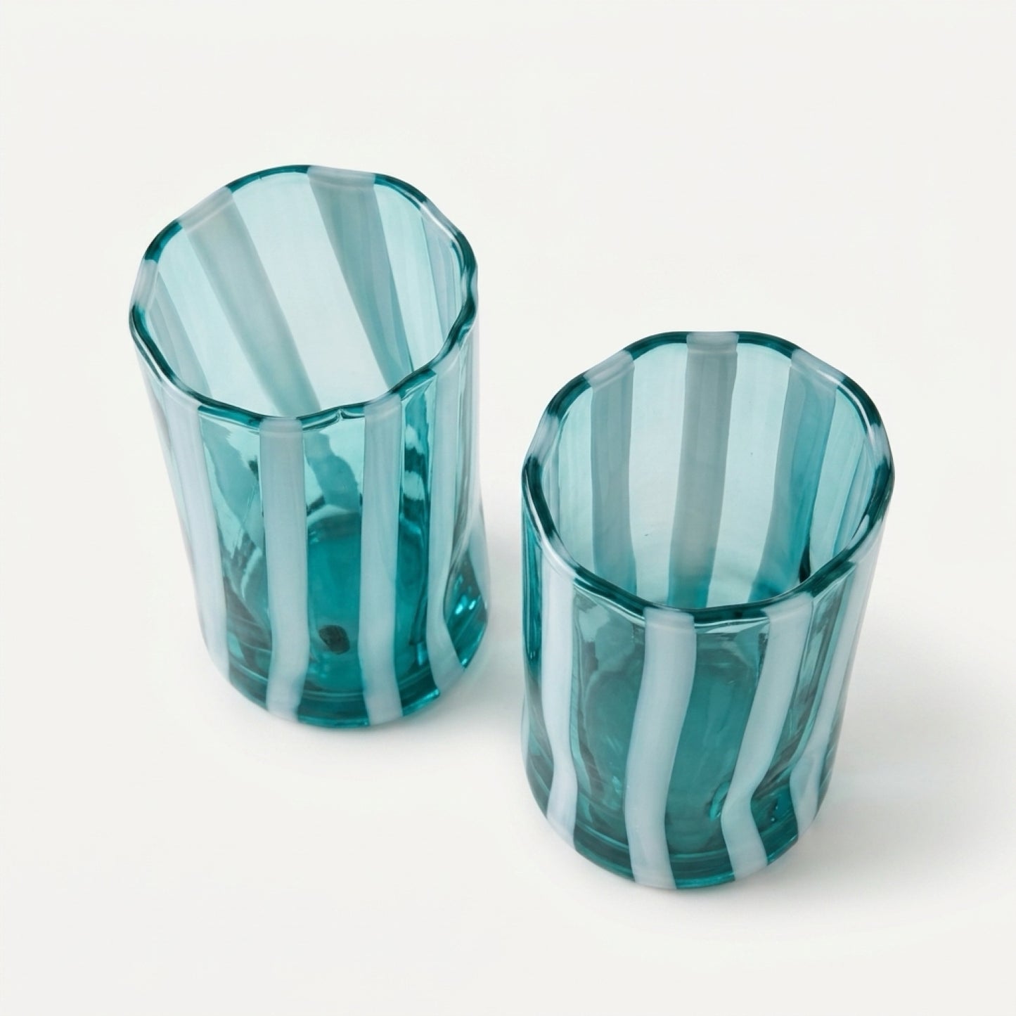 An overhead, high-angle view of a pair of Alessandro Coppola for Vetreria Arte di Murano hand-blown Italian glass tumblers, displaying their aqua and milk-white vertical candy stripes against a clean, crisp neutral background.