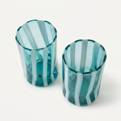An overhead, high-angle view of a pair of Alessandro Coppola for Vetreria Arte di Murano hand-blown Italian glass tumblers, displaying their aqua and milk-white vertical candy stripes against a clean, crisp neutral background.